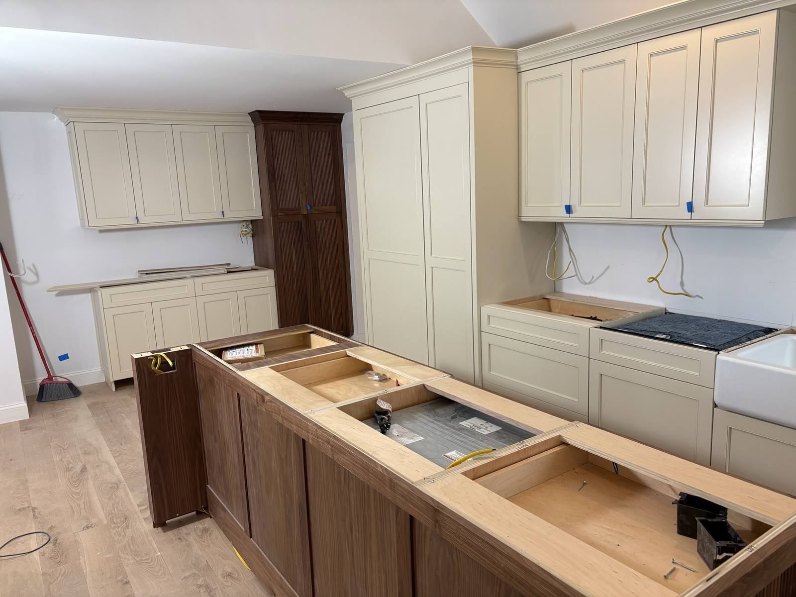 Cabinets going in: Painted perimeter cabinets and tall paneled cabinetry set, with the walnut island boxes in place before the counters.