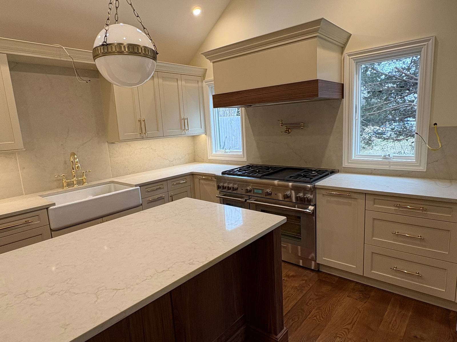 Range wall: A professional gas range under a paneled hood with a walnut band, beside a farmhouse sink with a brass faucet.