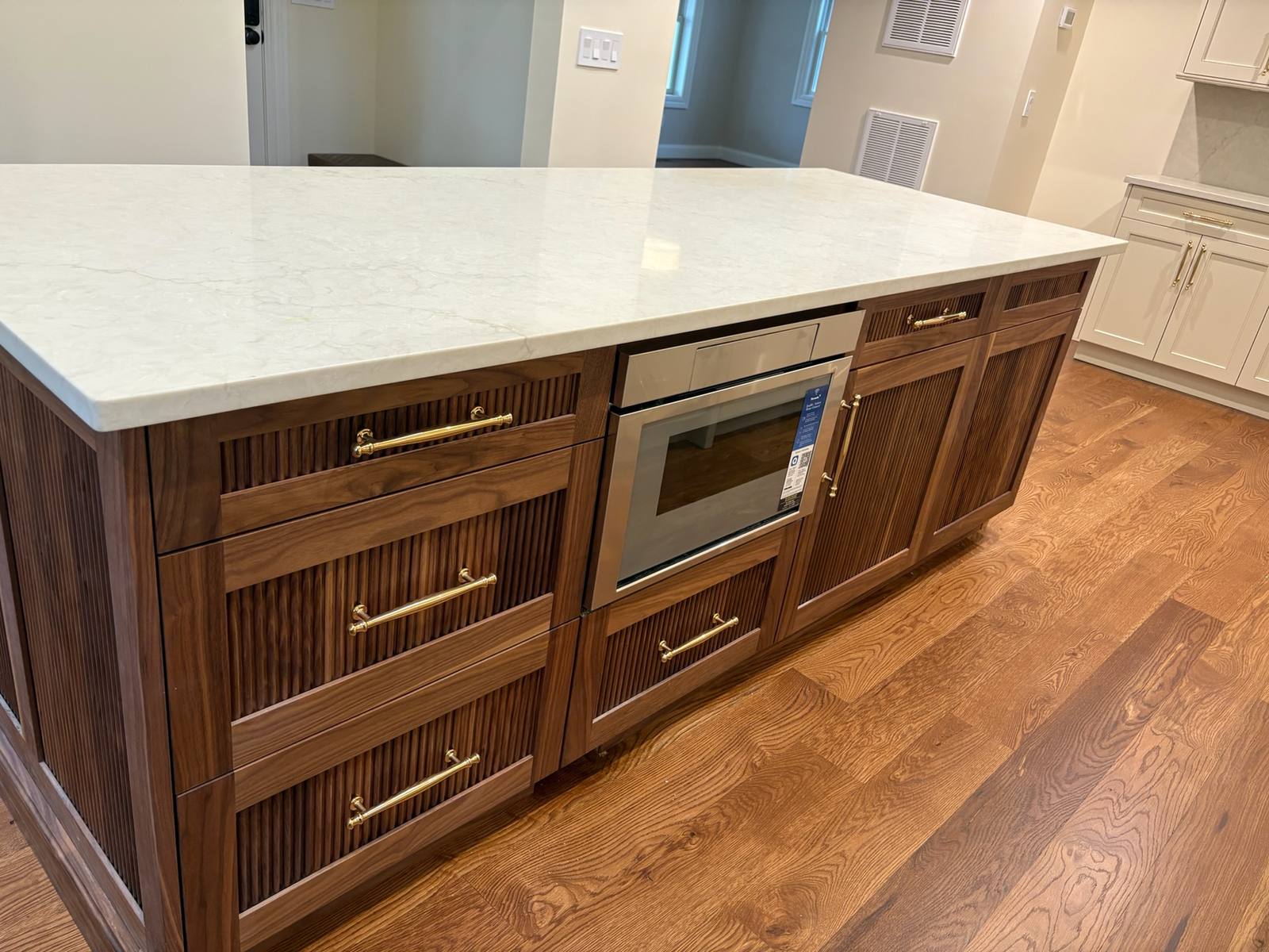 Island detail: Fluted walnut drawer fronts with brass pulls and a built in microwave drawer under the quartz top.