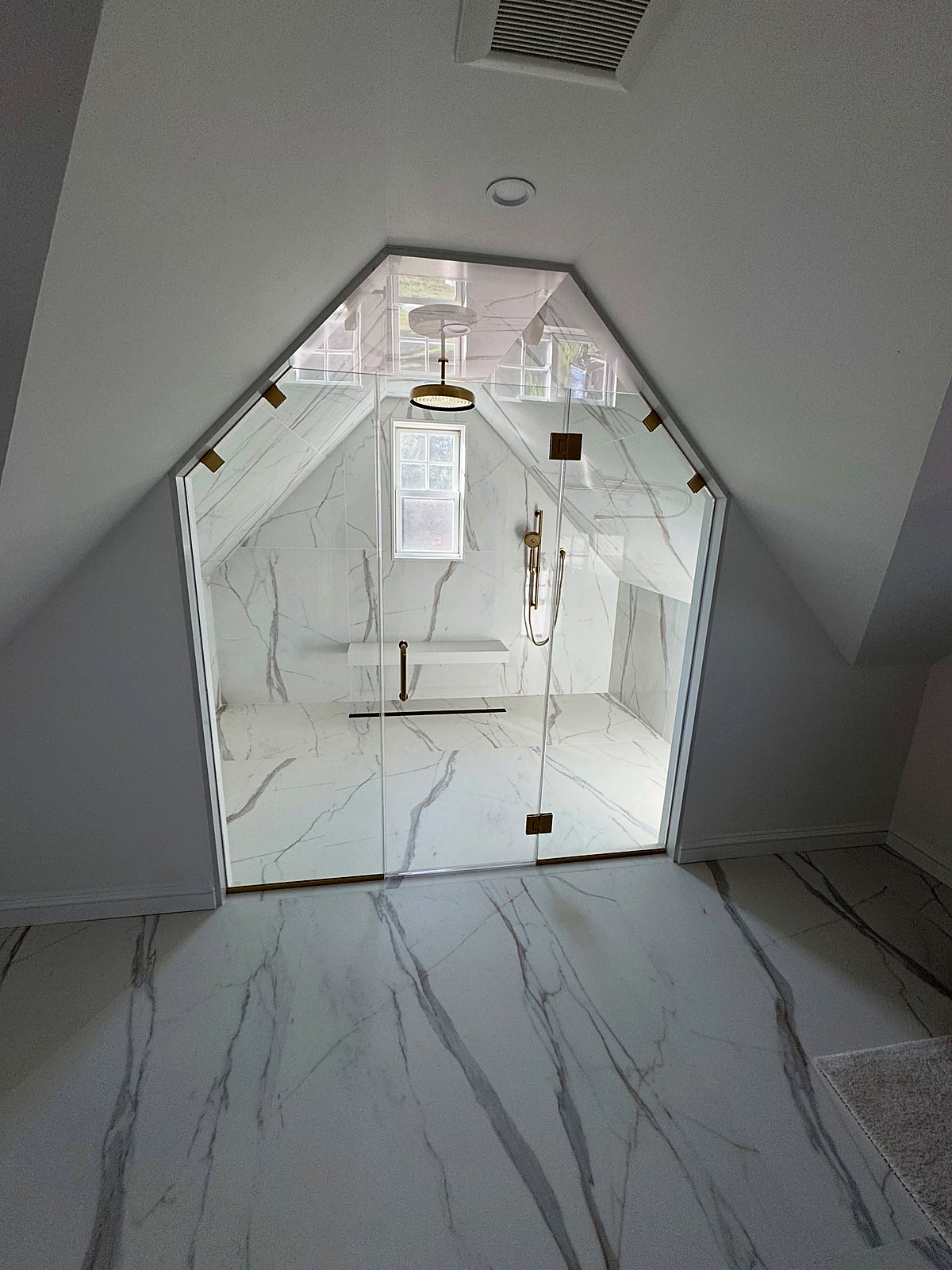 Attic steam shower with a peaked glass enclosure, white marble, and gold fixtures
