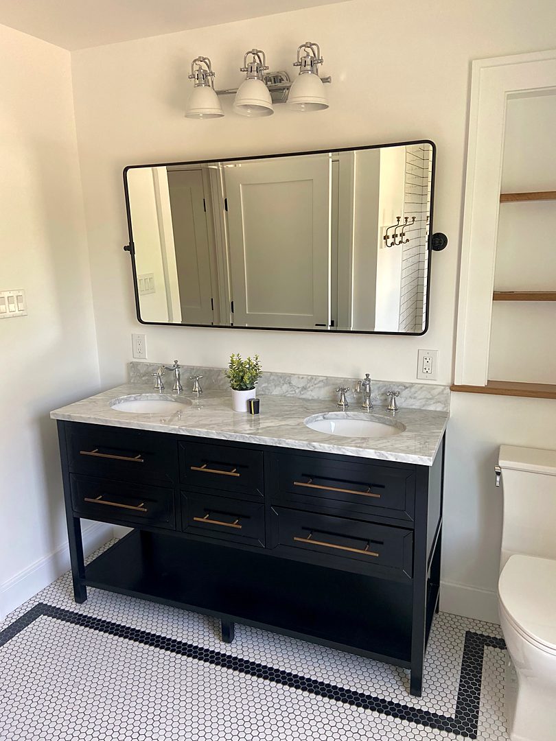 Black double vanity with a marble top, brass pulls, and a penny tile floor with a black border