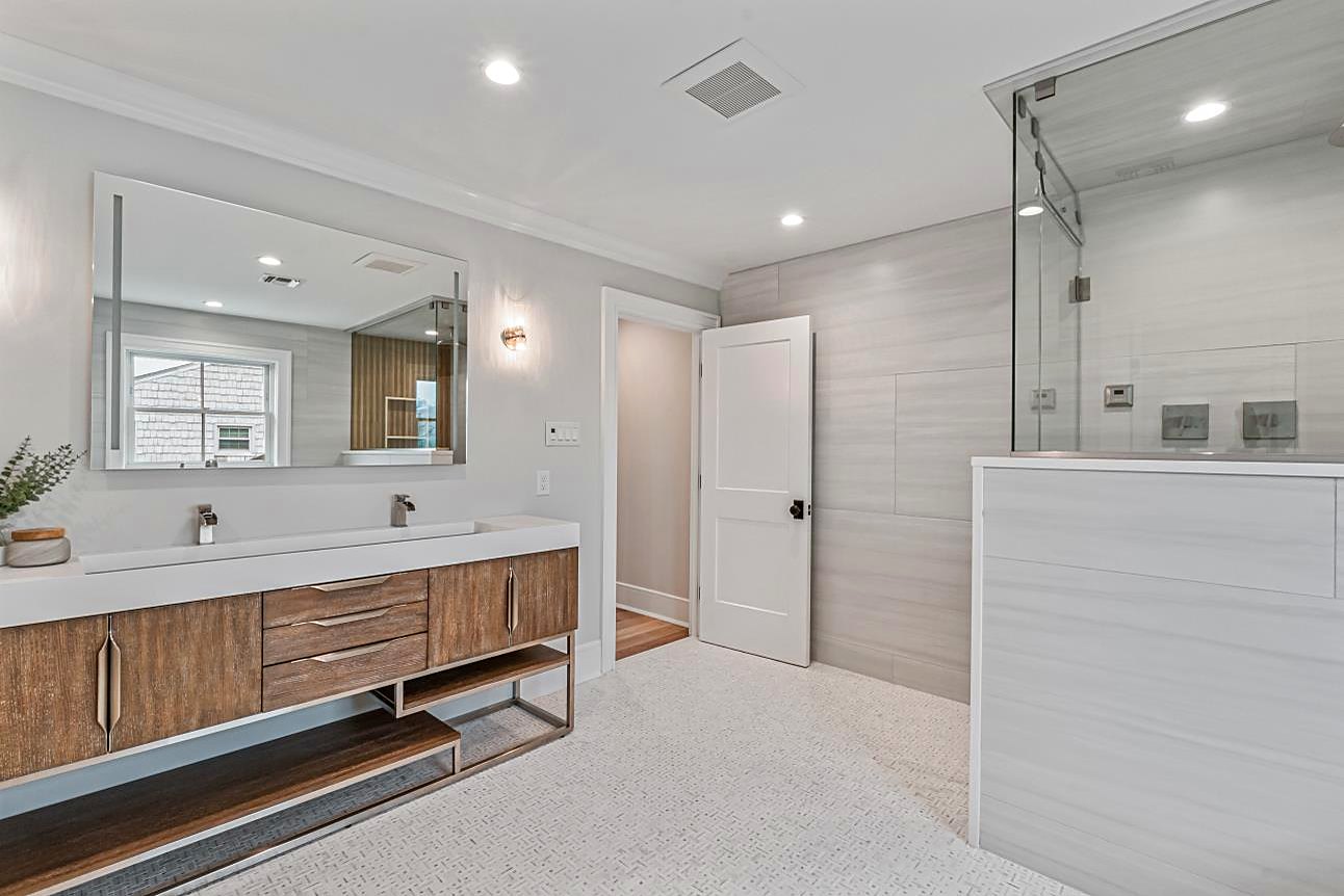 Bathroom with a floating walnut double vanity, a trough sink, and a walk-in shower