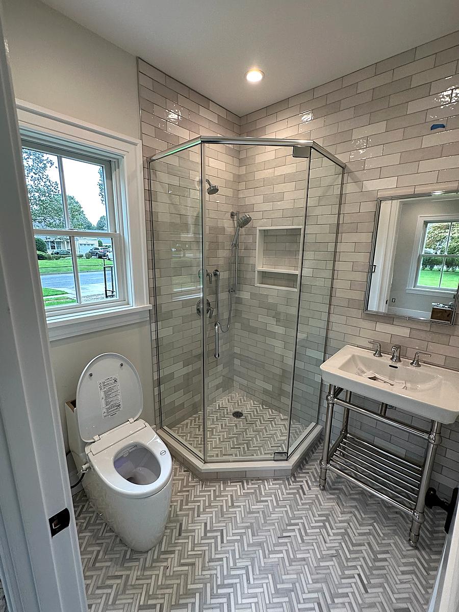 Glass corner shower with marble tile and a window above the vanity