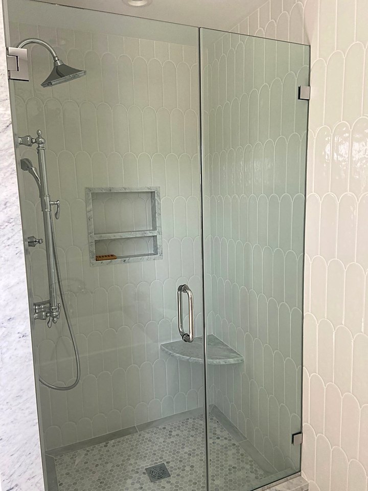 Frameless glass shower with white tile, a niche, and a pebble floor