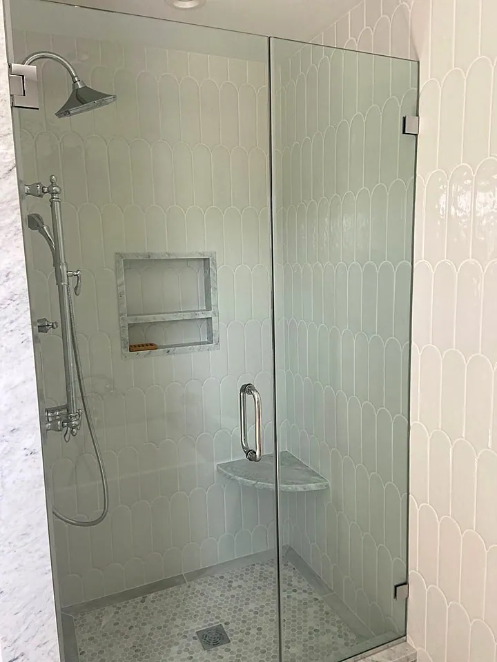 Frameless glass shower with white tile, a niche, and a pebble floor