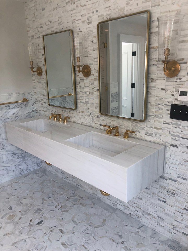 Bathroom with a floating marble double vanity, brass fixtures, and marble mosaic walls