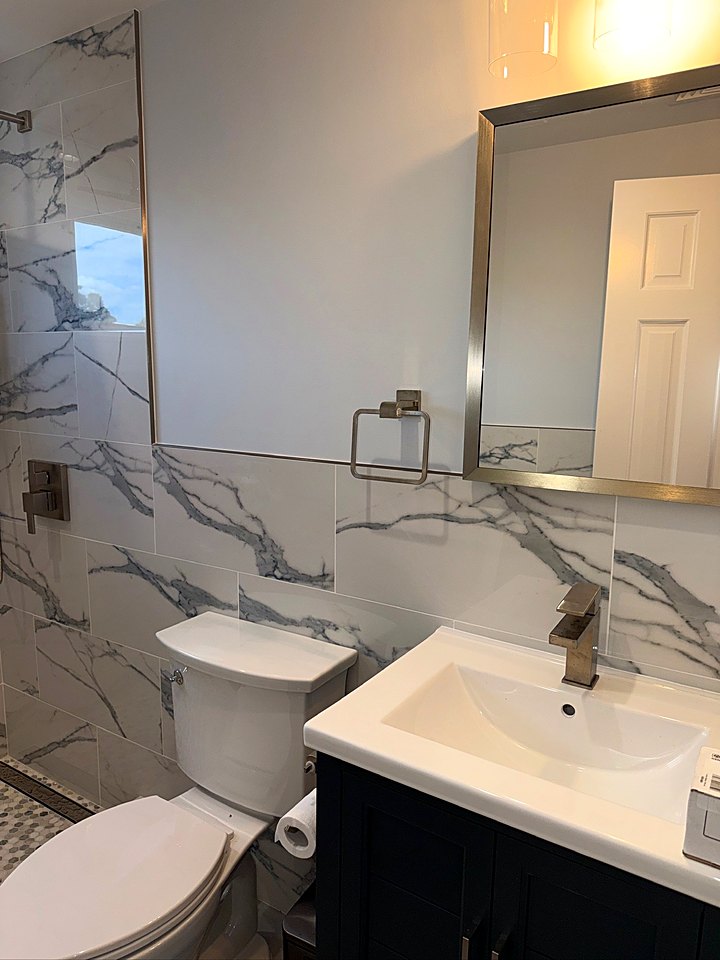 Bathroom with marble-look tile walls, a navy vanity, and a framed mirror