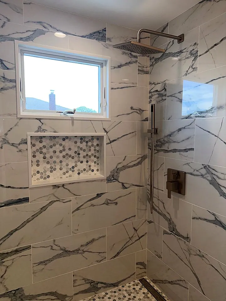 Shower with bold marble-look tile, a pebble mosaic niche, and a window