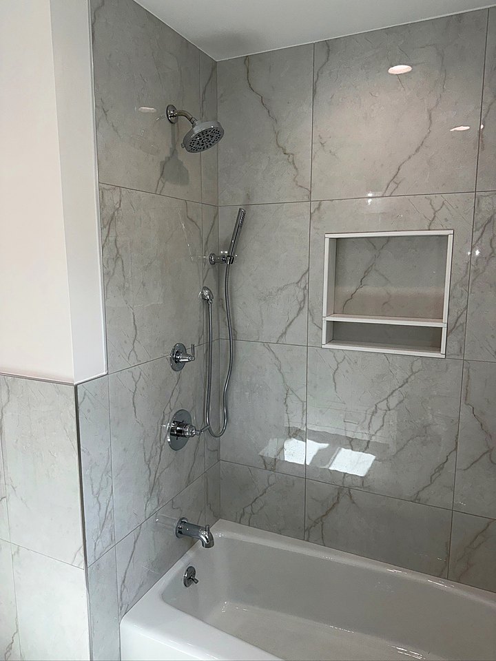 Tub and shower with large marble-look tile, a recessed niche, and a handheld shower