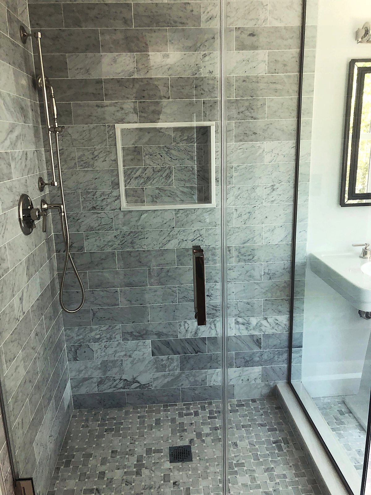 Gray marble subway tile shower with a glass door and a built-in niche