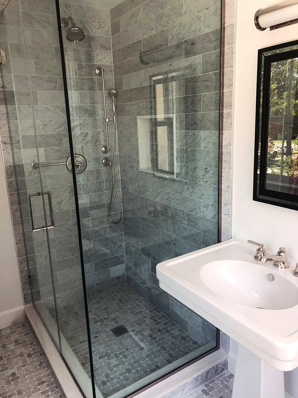 Gray marble shower with a pedestal sink and a black framed mirror