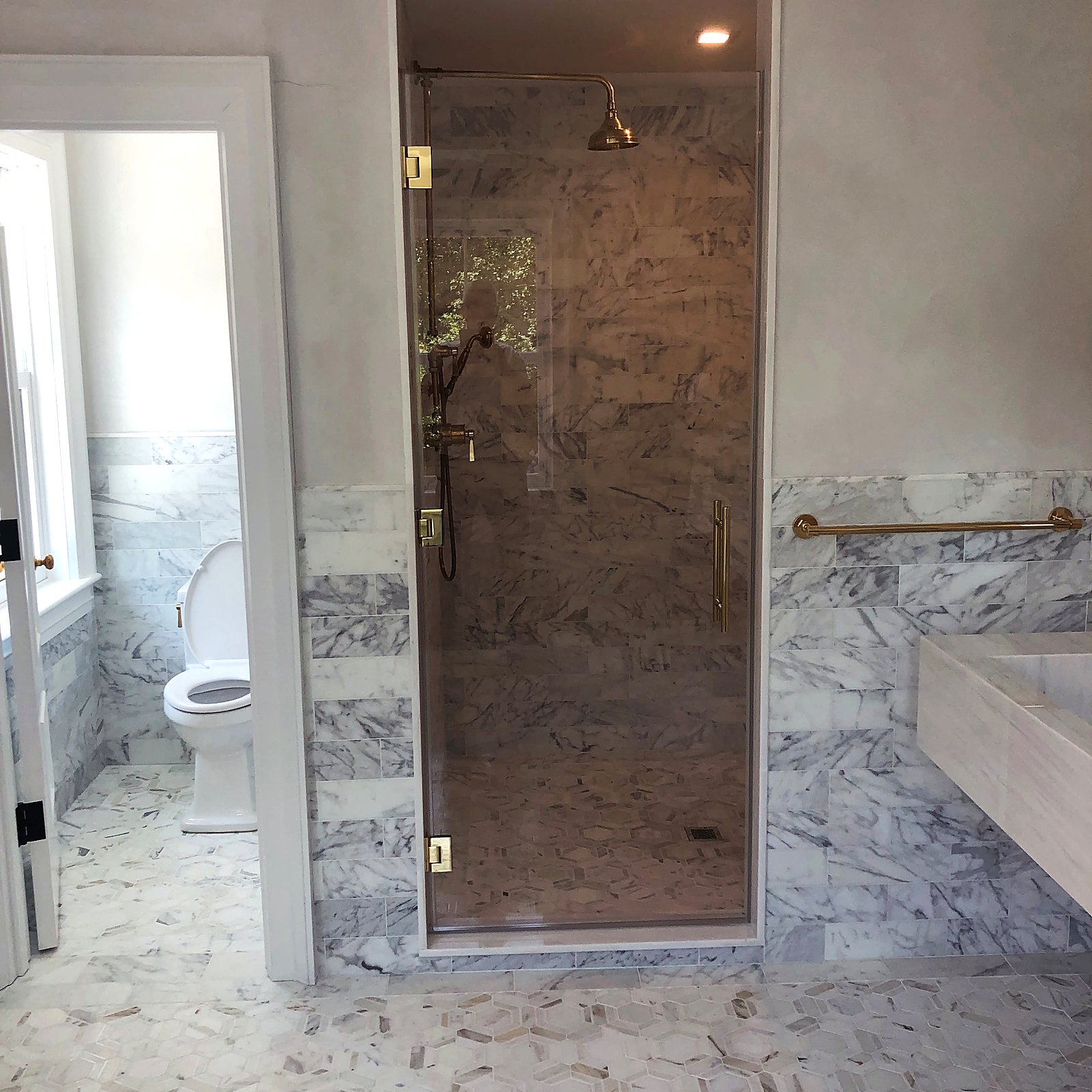 Marble bathroom with a glass shower and a brass rainfall shower head