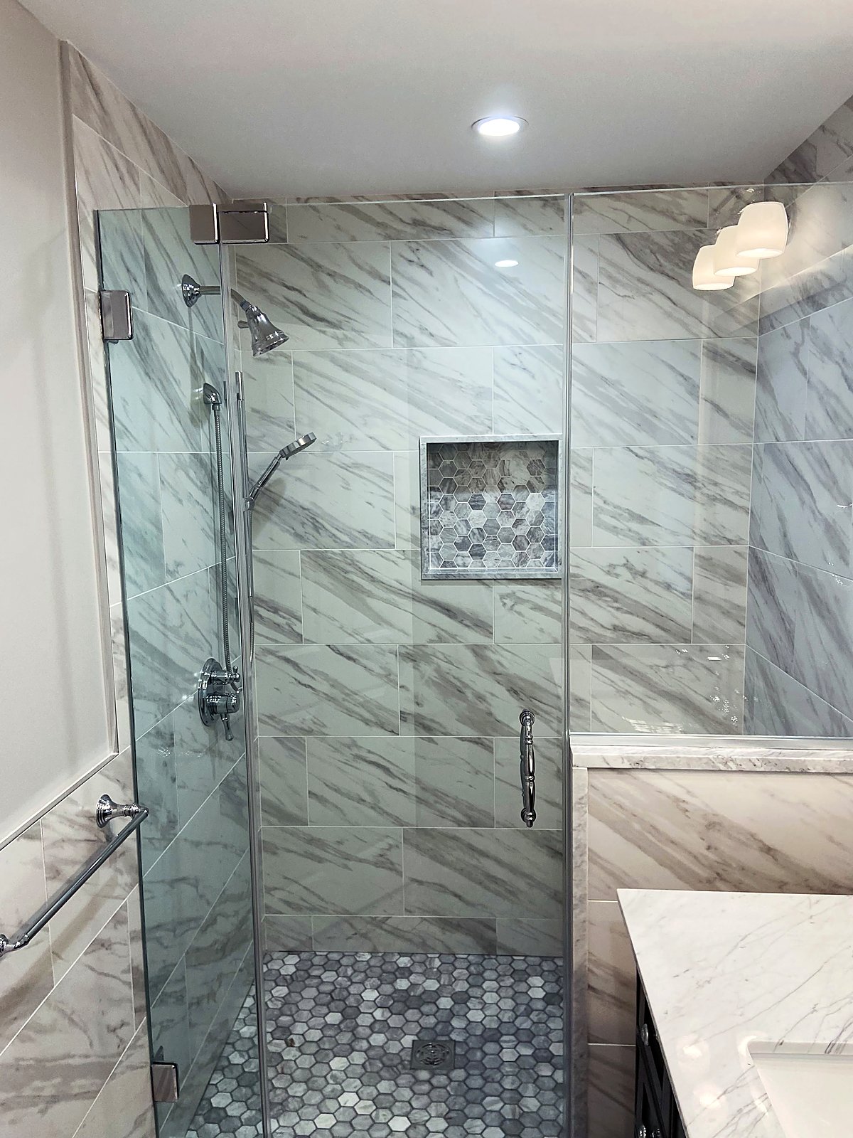 Marble shower with a glass enclosure and a hexagon tile accent niche