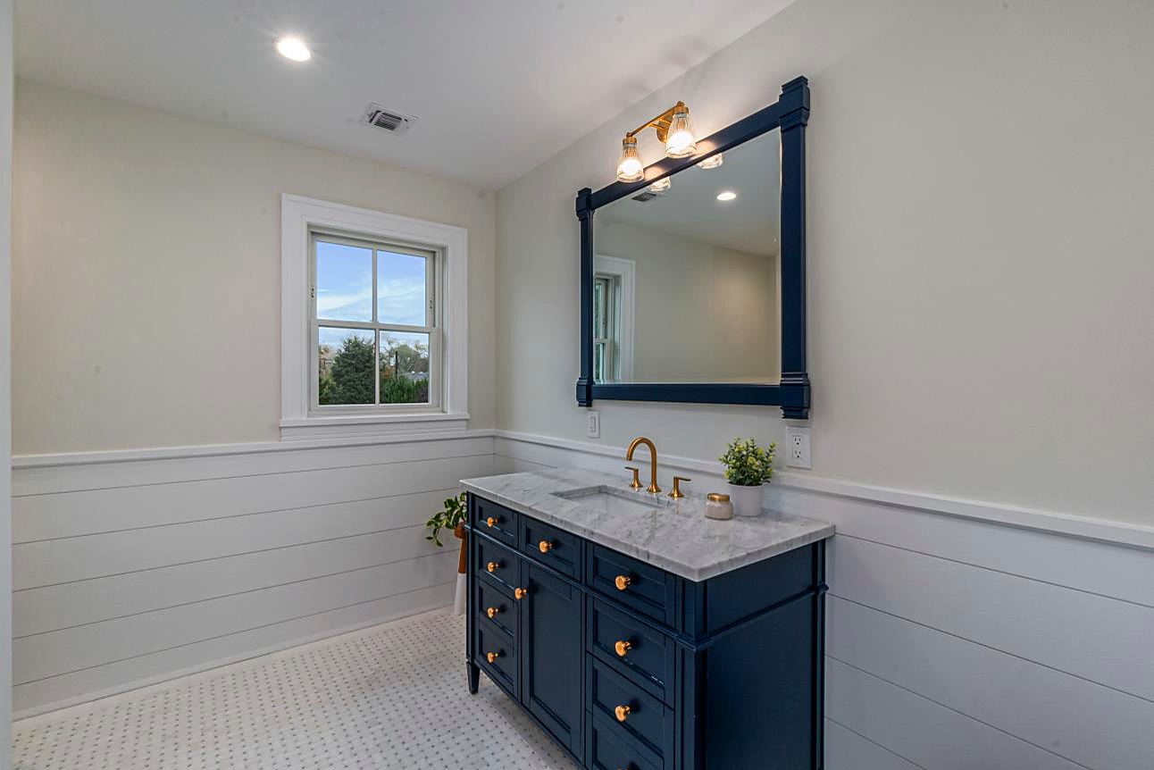 Bathroom with a navy vanity, a marble top, brass fixtures, and white shiplap walls