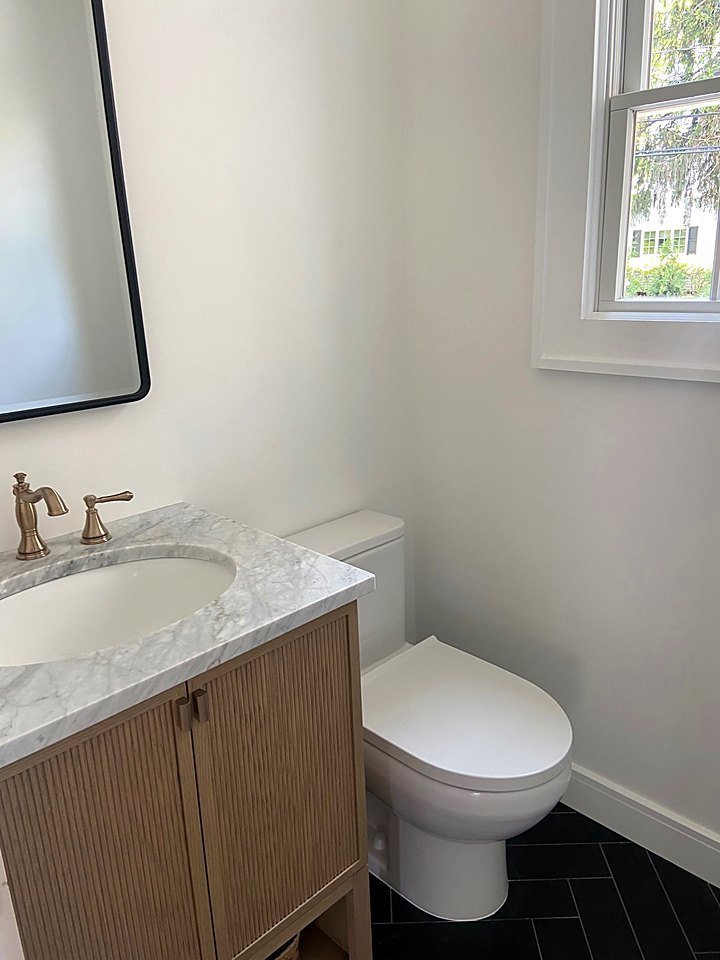 Powder room with a wood vanity, marble top, brass faucet, and black floor tile