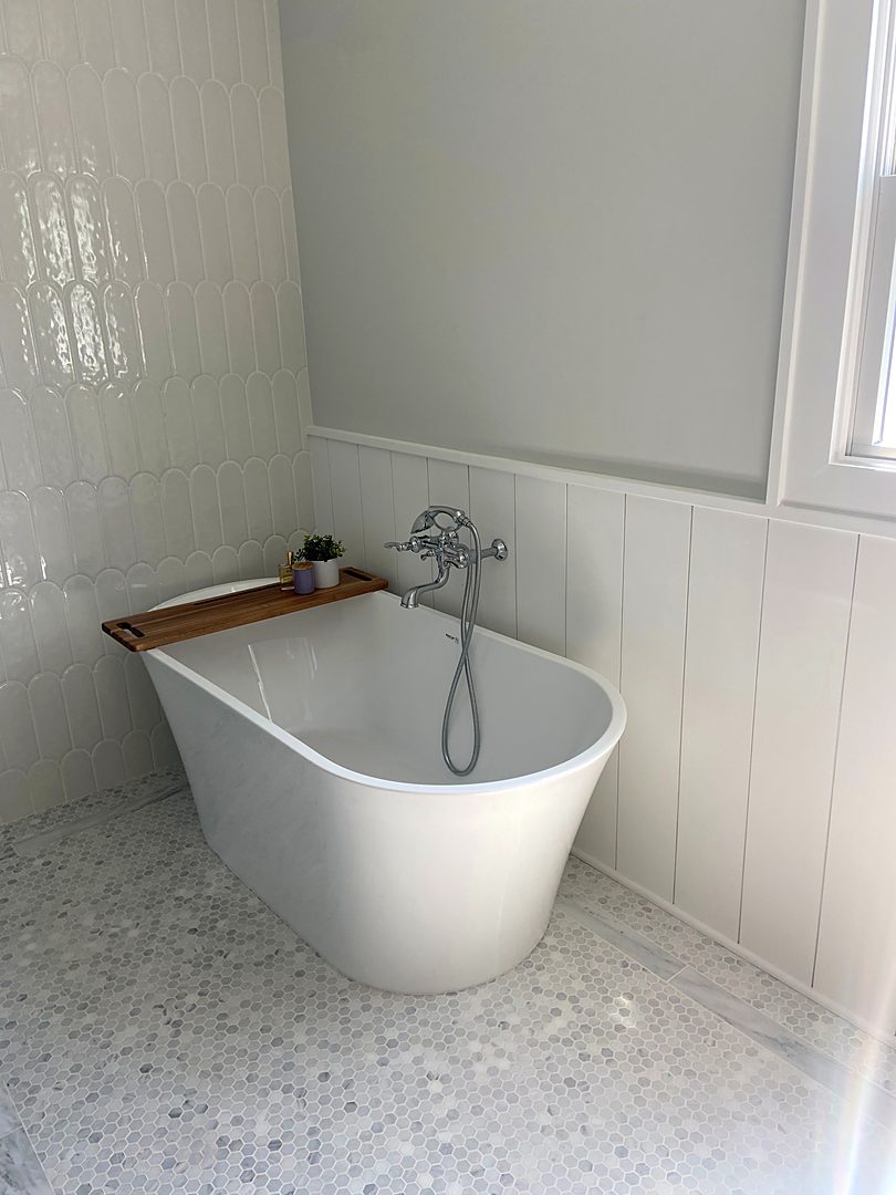 Freestanding soaking tub with a wall-mounted filler, white tile wainscot, and a marble mosaic floor