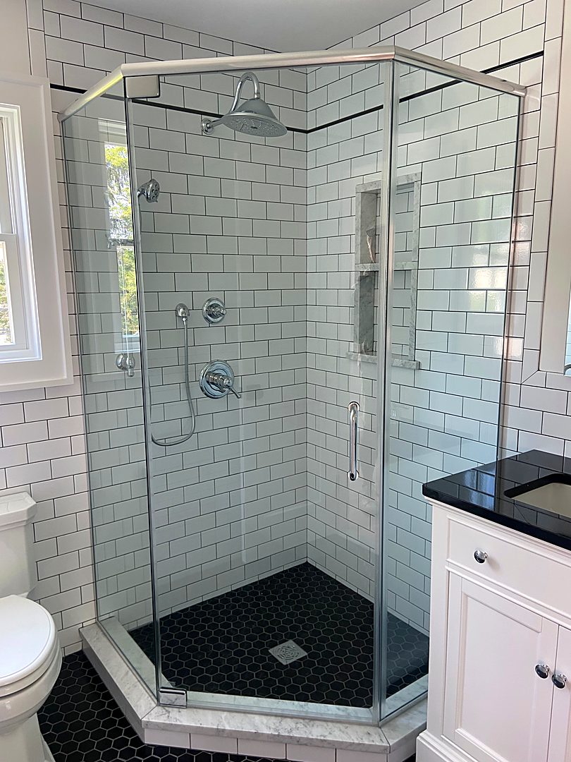 Neo-angle glass shower with white subway tile, a niche, and a black hex tile floor