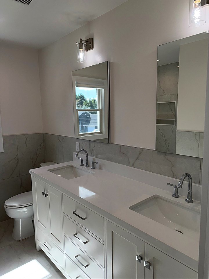 White double vanity with a quartz top and twin mirrors under a window