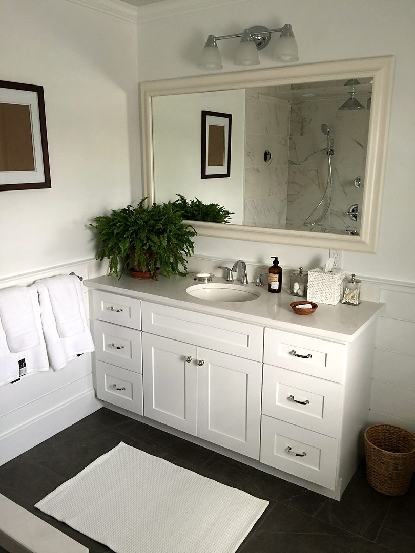 White shaker vanity with a framed mirror and white wainscoting in a bright bathroom