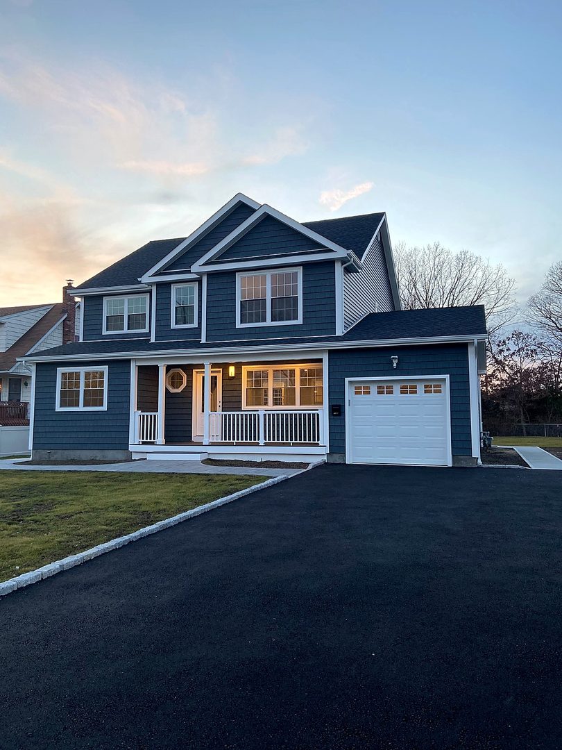 Finished blue shingle-sided home at dusk with a covered front porch and attached garage