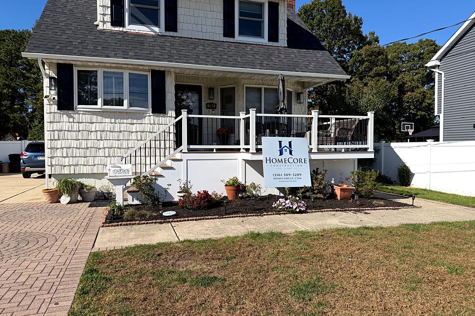 Front of the house with the new porch, a white railing, and fresh plantings along the paver walk