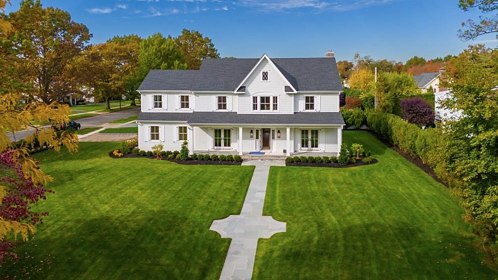 Aerial view of a white custom farmhouse with a front porch and a long front walkway