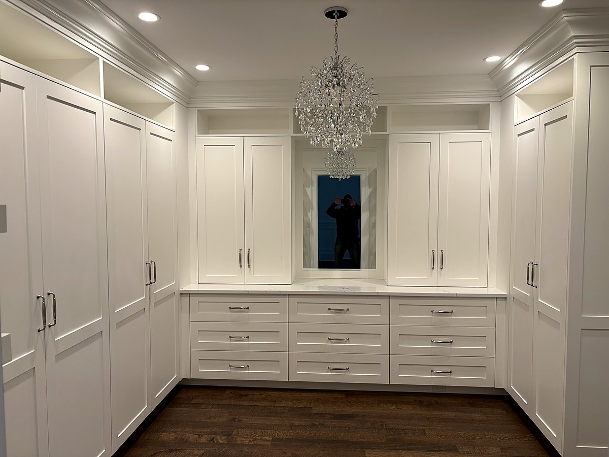 Dressing room lined with white built-in wardrobes and a drawer bank