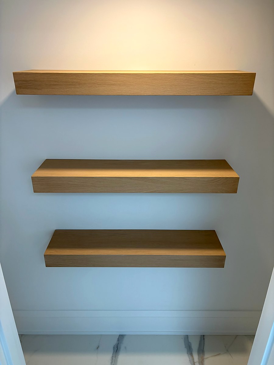 Three floating white oak shelves mounted on a painted wall