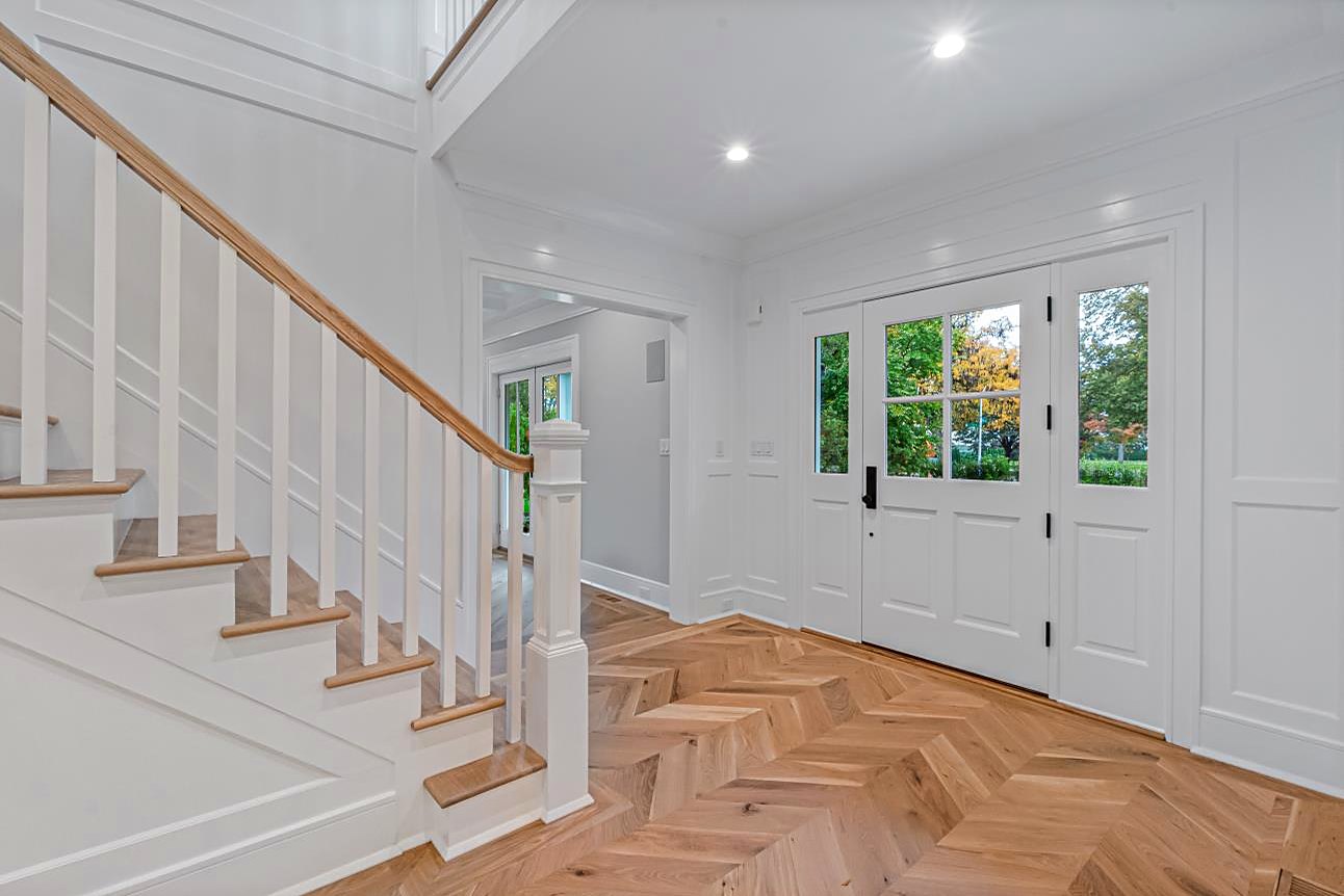 Foyer with a curved staircase, a glass-paneled front door, and herringbone floors