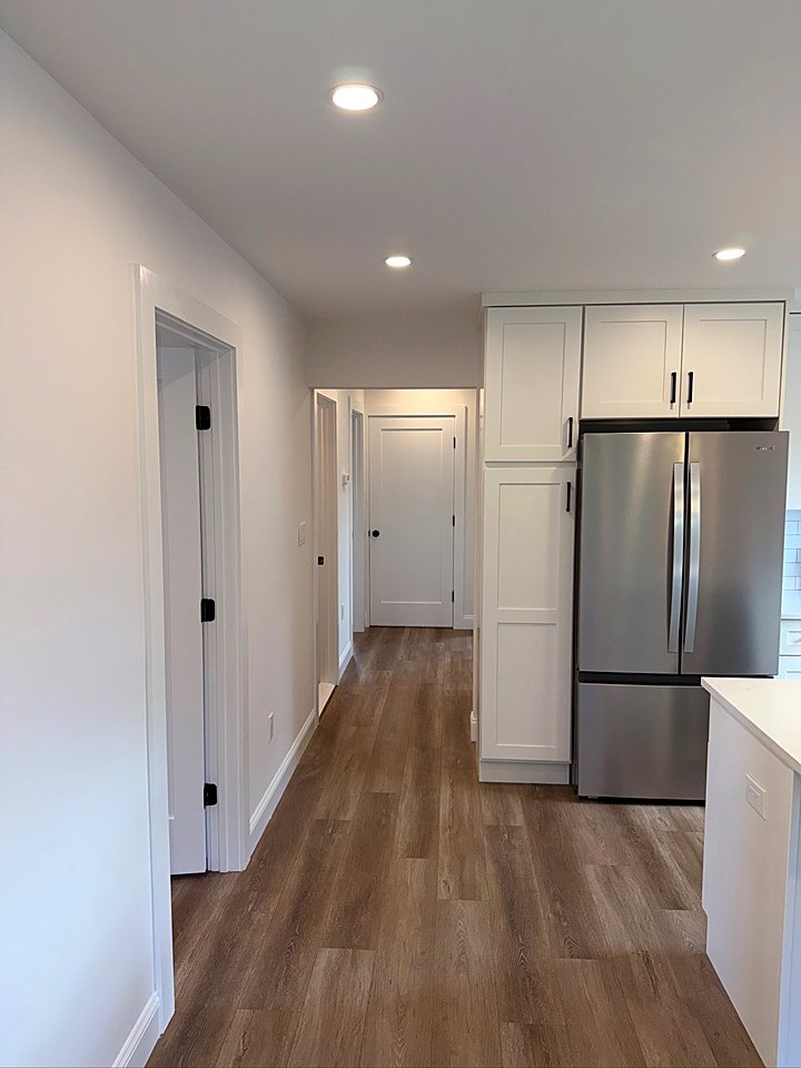 Bright hallway with new plank flooring leading to a white kitchen