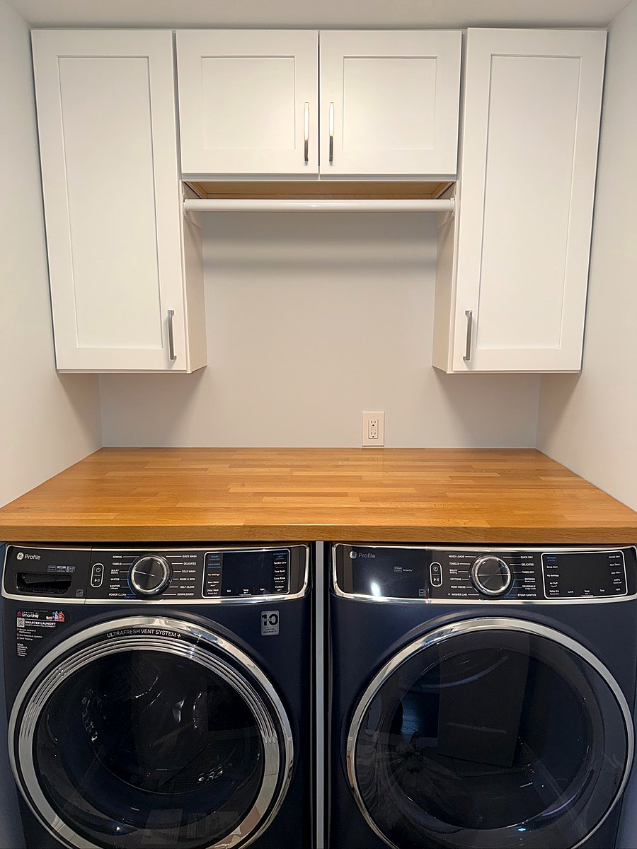 Laundry room with white upper cabinets above a butcher block folding counter