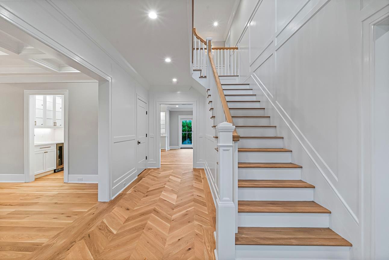 Entry hall with a white oak staircase, wainscoting, and herringbone wood floors