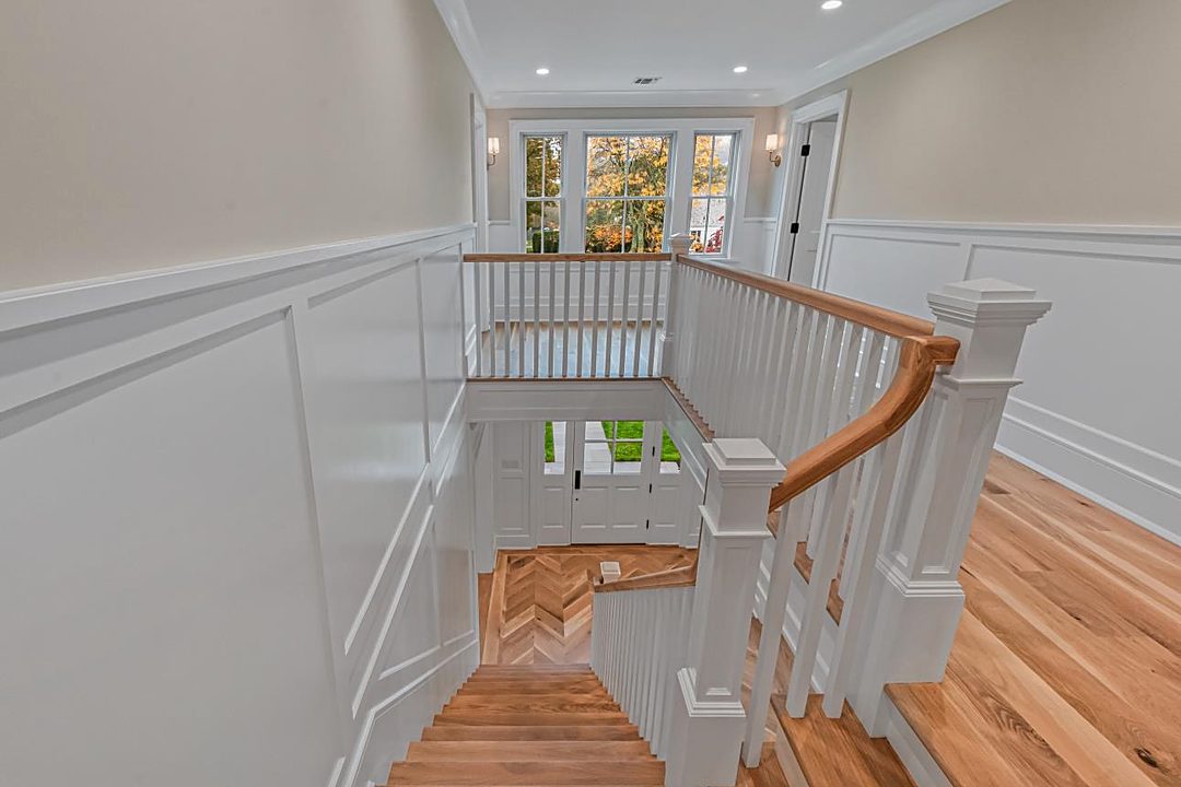 Upstairs landing with a white oak railing, wainscoting, and a view down the stairwell