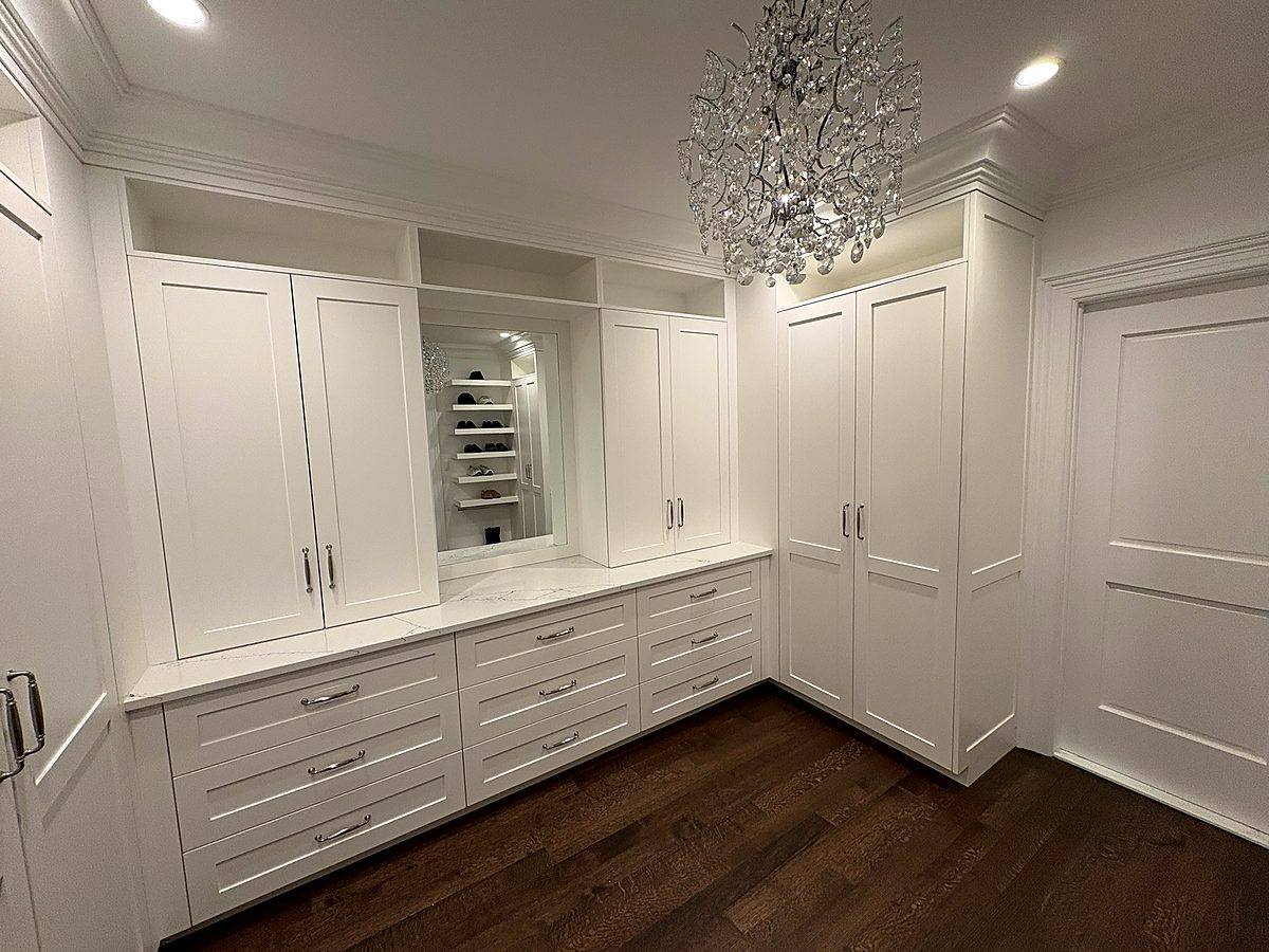 Walk-in closet with white built-in cabinetry and a crystal chandelier