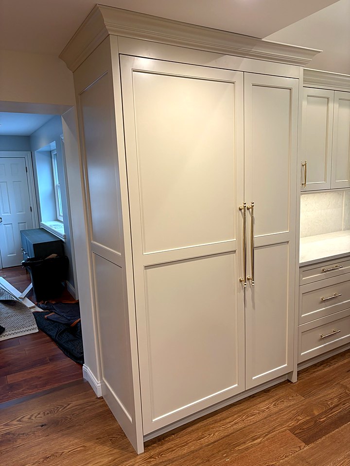 Paneled refrigerator built into white cabinetry with brass pulls