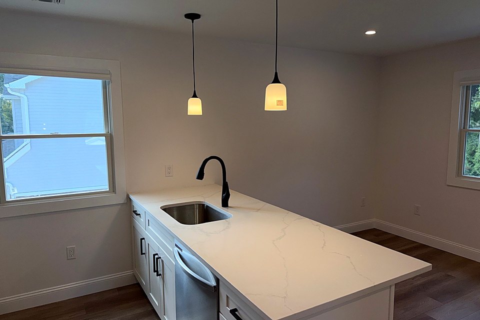 White kitchen with a quartz peninsula, undermount sink, and twin pendant lights