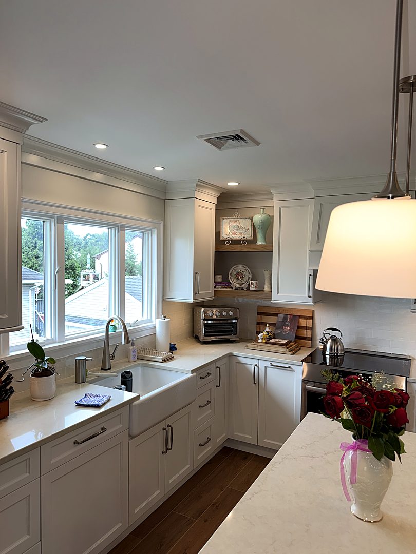 White shaker kitchen with a farmhouse sink, quartz counters, and a corner display shelf