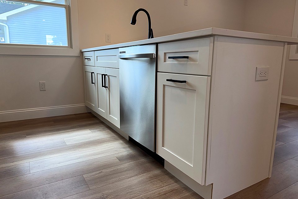 White shaker cabinets with a stainless dishwasher and a black faucet by the window