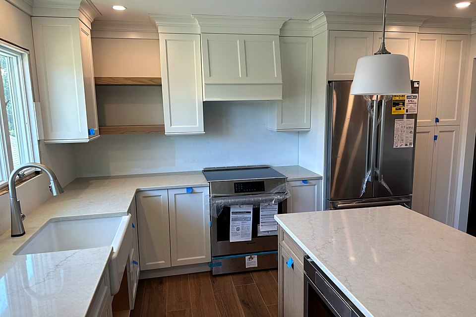 White kitchen with a large quartz island, open shelving, and a stainless range
