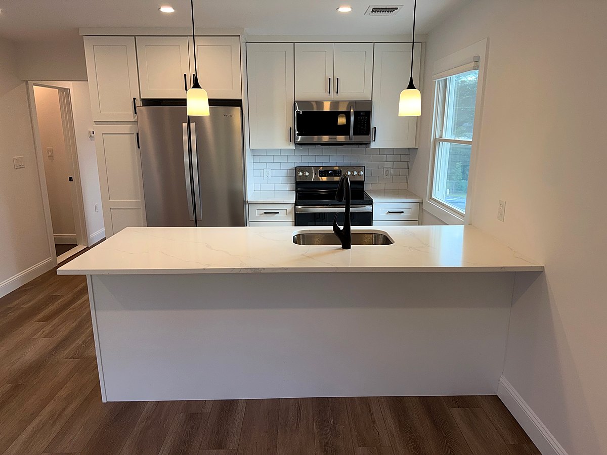 Wide quartz island in a white shaker kitchen with wood floors