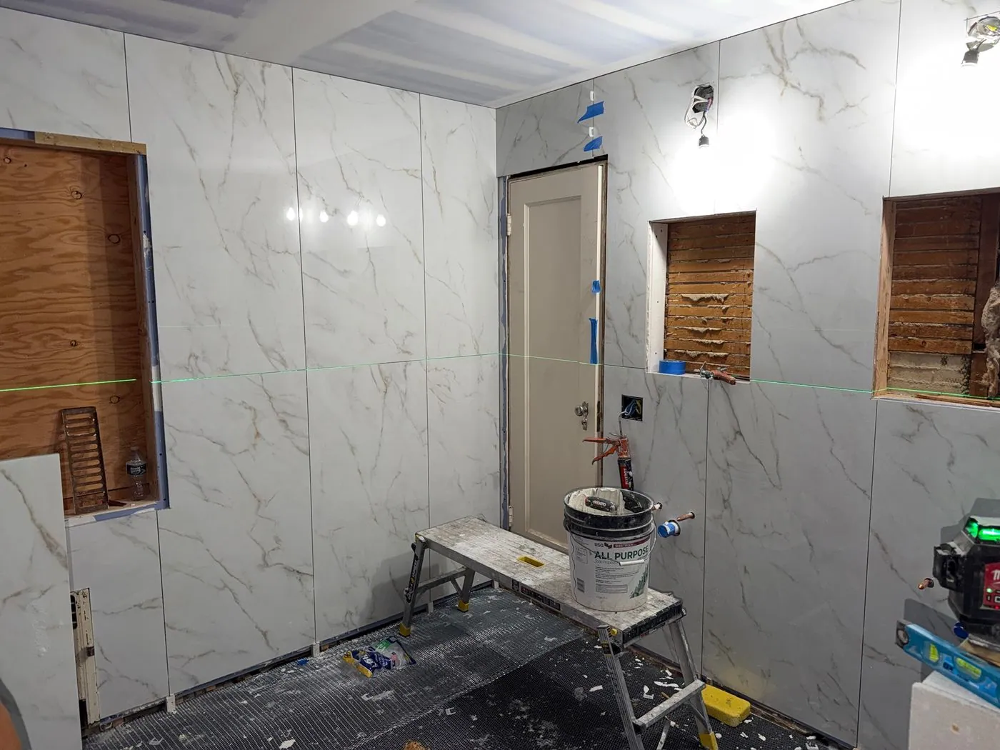Wall tile going up: Large format marble look tile on the walls, with a laser level set up.