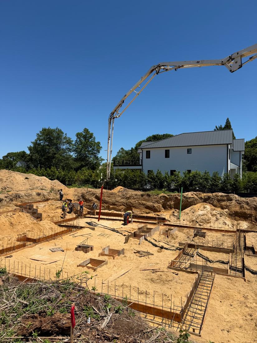 Footing forms set: Footing forms and rebar set in the excavation, with the pump truck boom moving into position.