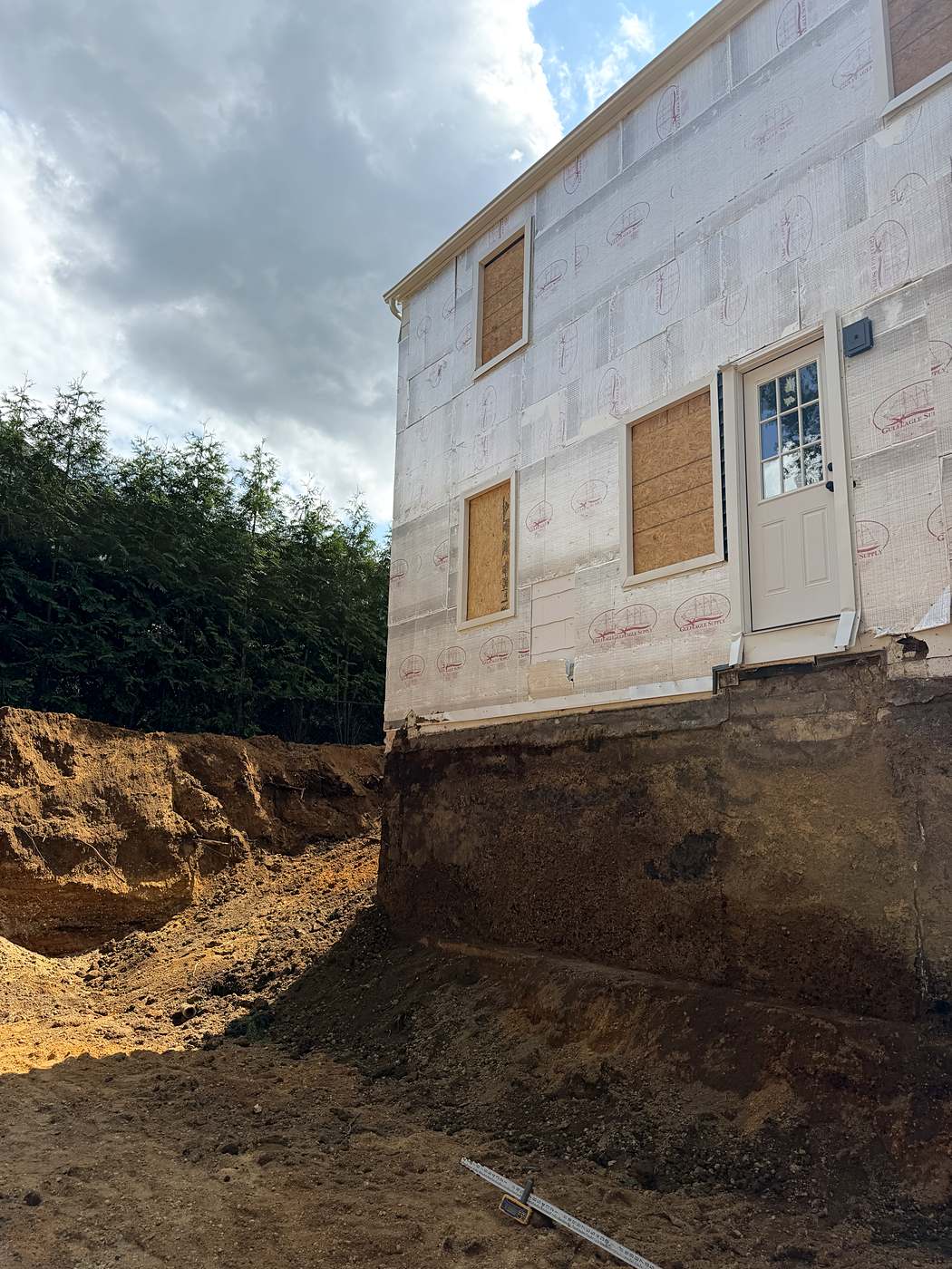 The house standing at the edge of the open excavation for the new foundation