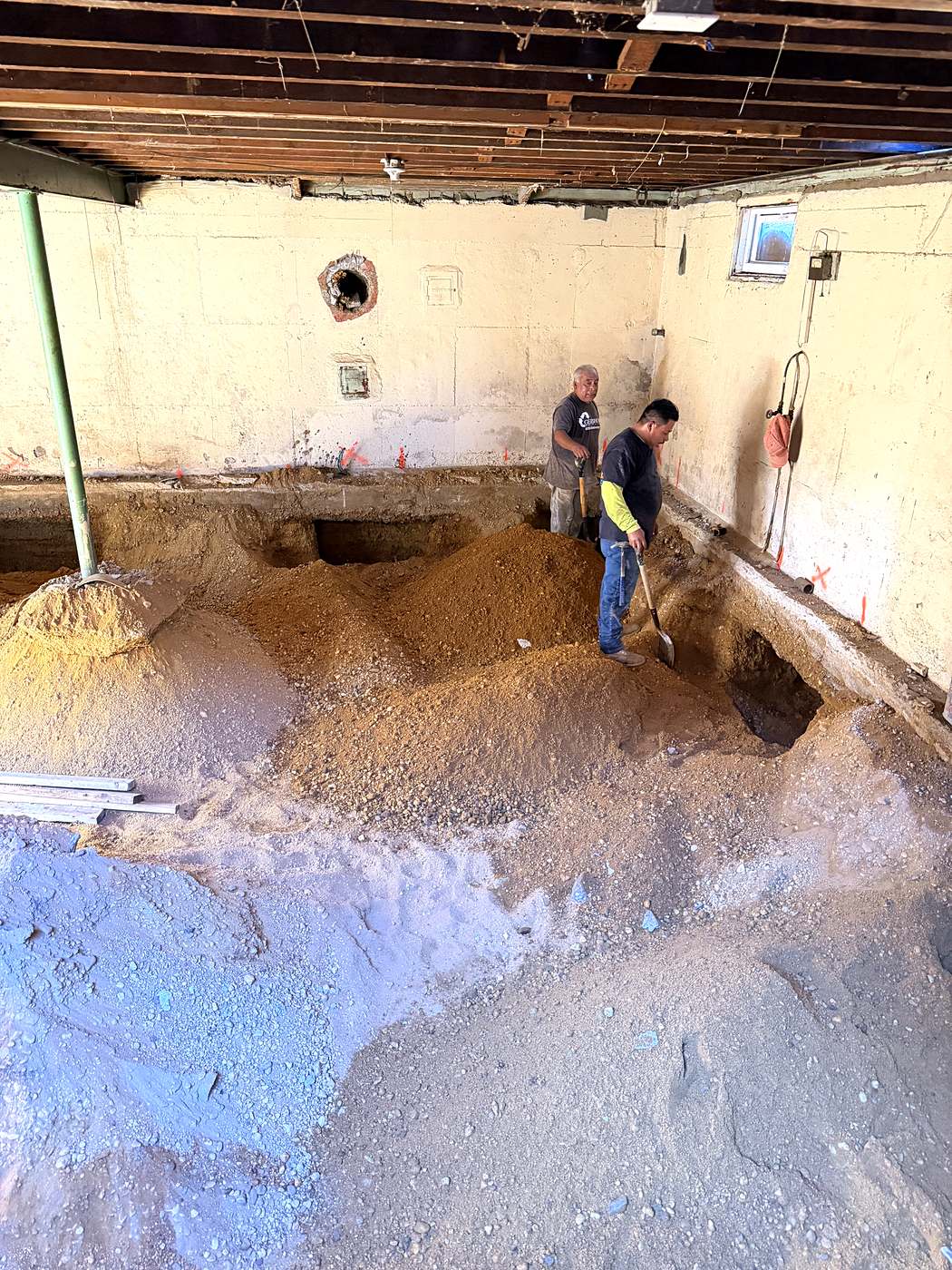 Two crew members digging out the basement by hand beneath the supported house