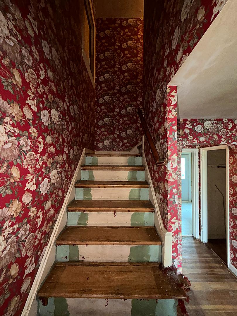 Original staircase with worn treads and floral wallpaper before the renovation