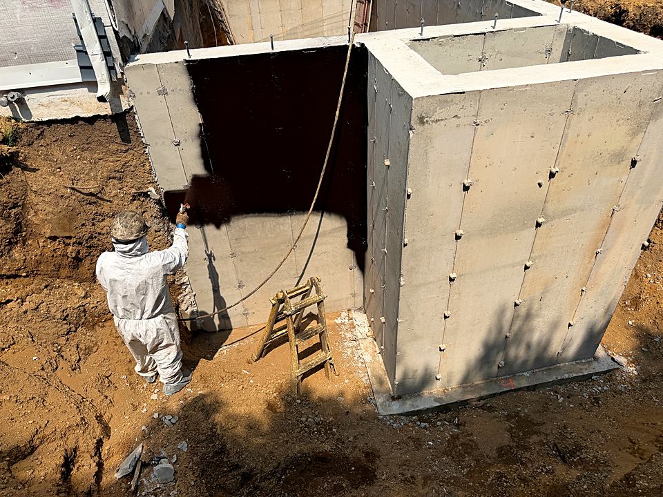 Crew member spraying waterproofing onto a newly poured foundation wall
