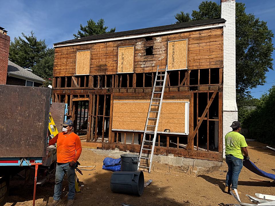 Crew at the back of the house with the siding stripped and the wall framing exposed