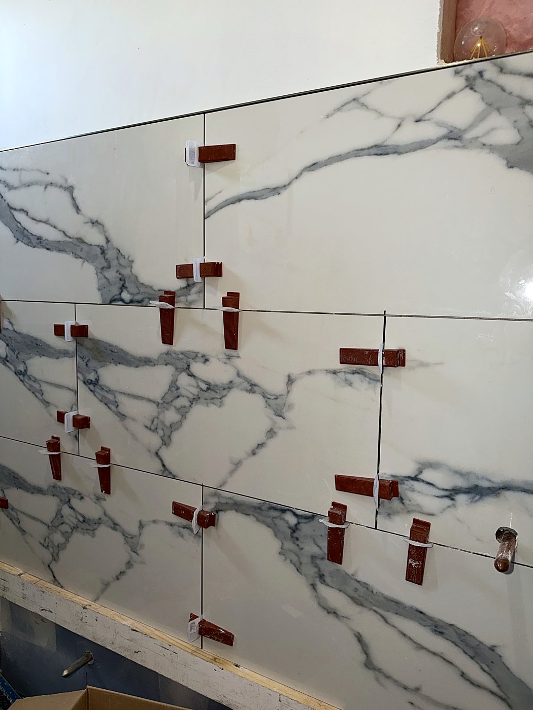 Close view of the veined marble tile with leveling clips set in the joints