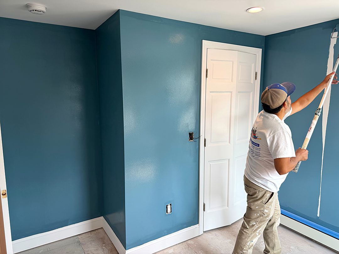Painter rolling a deep teal color onto a bedroom wall