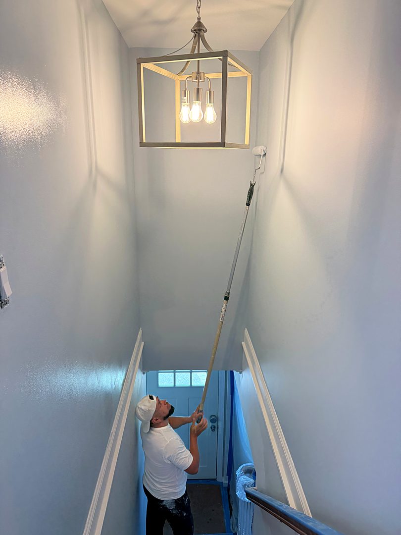 Painter working up a tall stairwell with an extension roller under a new pendant light